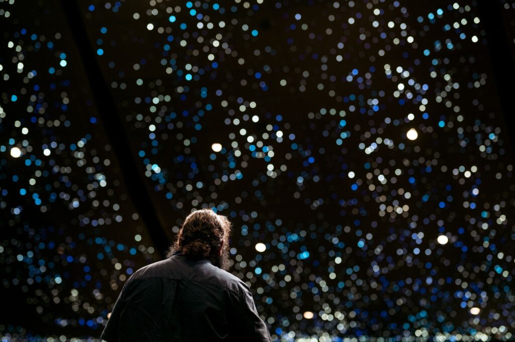 Figure with long dark hair looking towards a constellation of lights