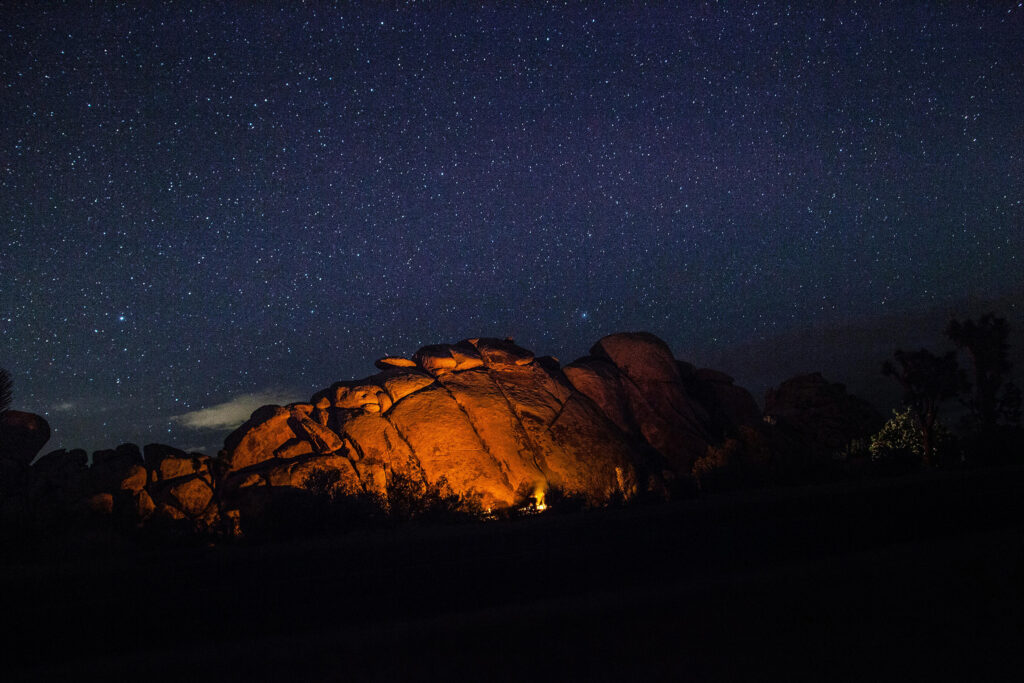 Dark landscape with starry sky and fire-lit rocky outcrop in the middle ground