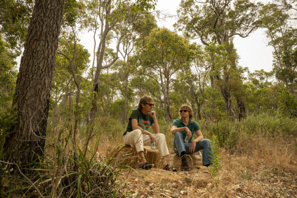 Two brothers in sunglasses sitting in the bush and looking reflective