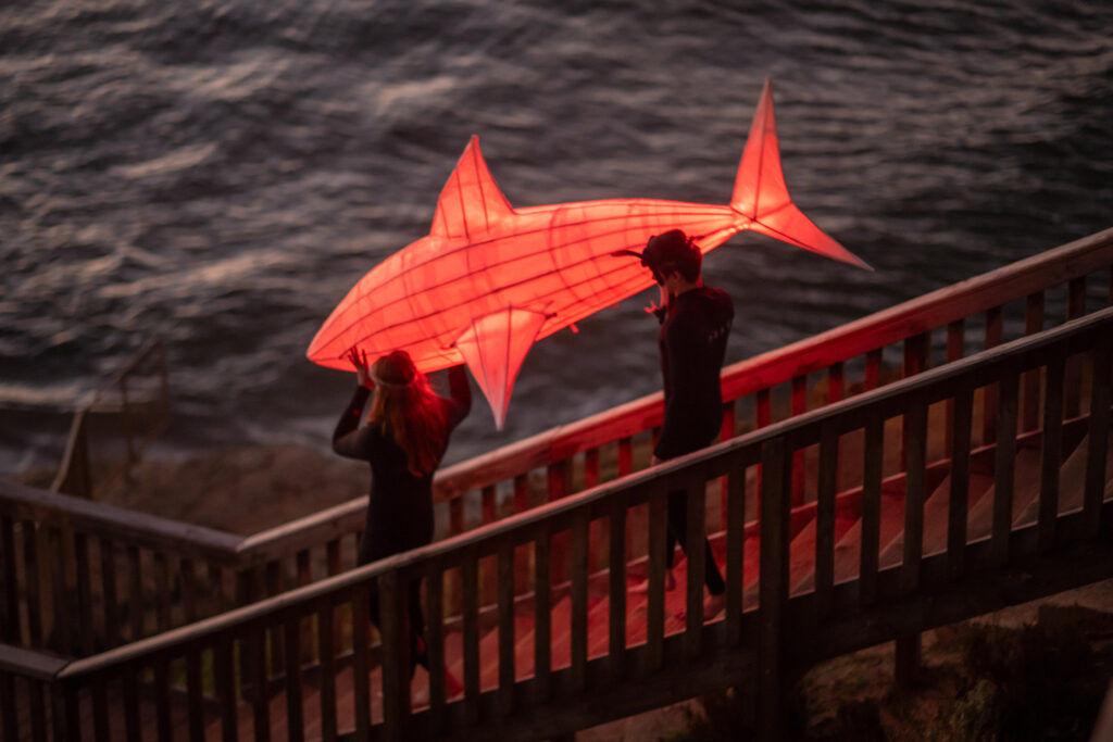 Shark lantern being carried down to the sea by two surfers on a boardwalk